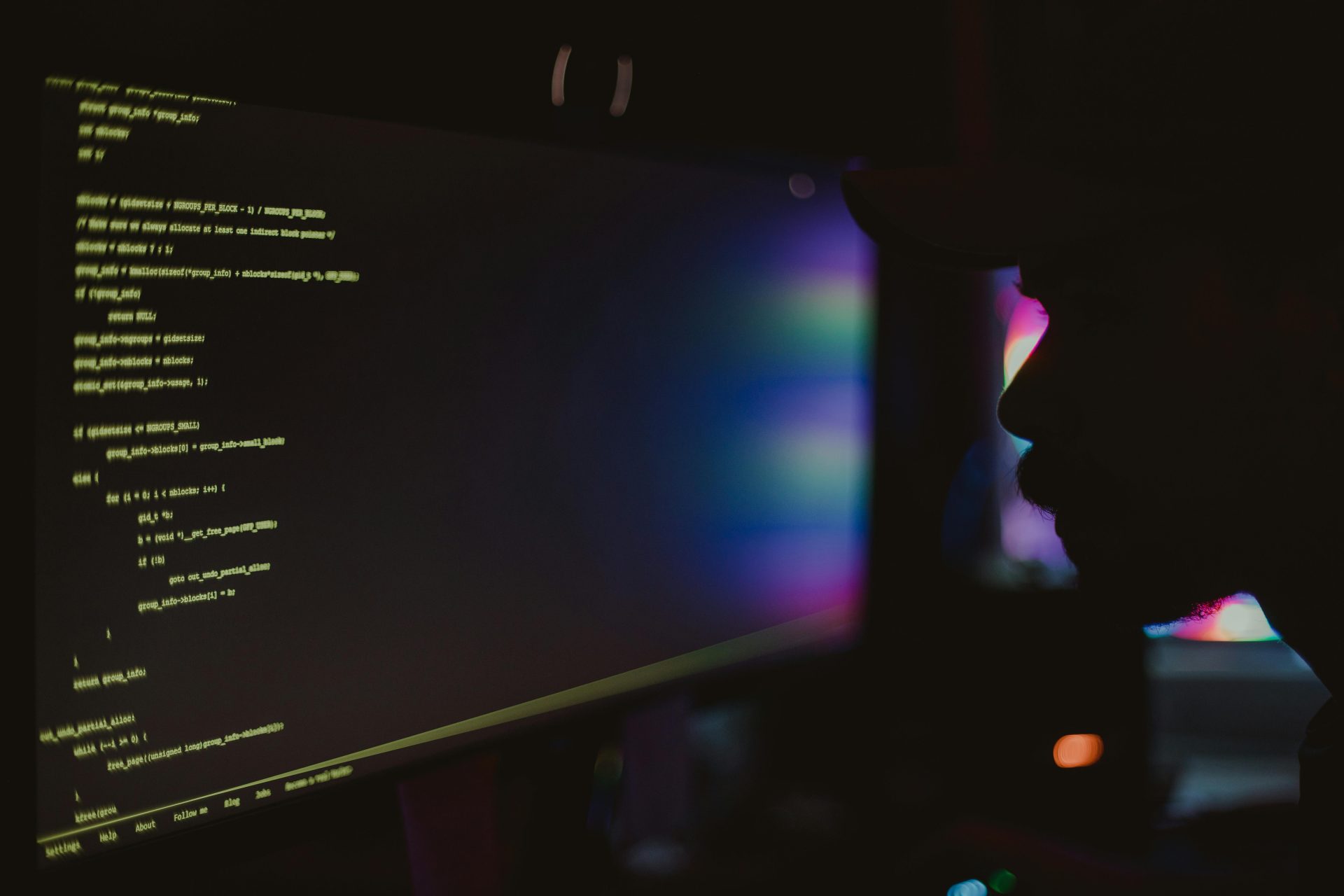 Silhouette of a programmer coding in a dark room, focusing on the screen with lines of code.